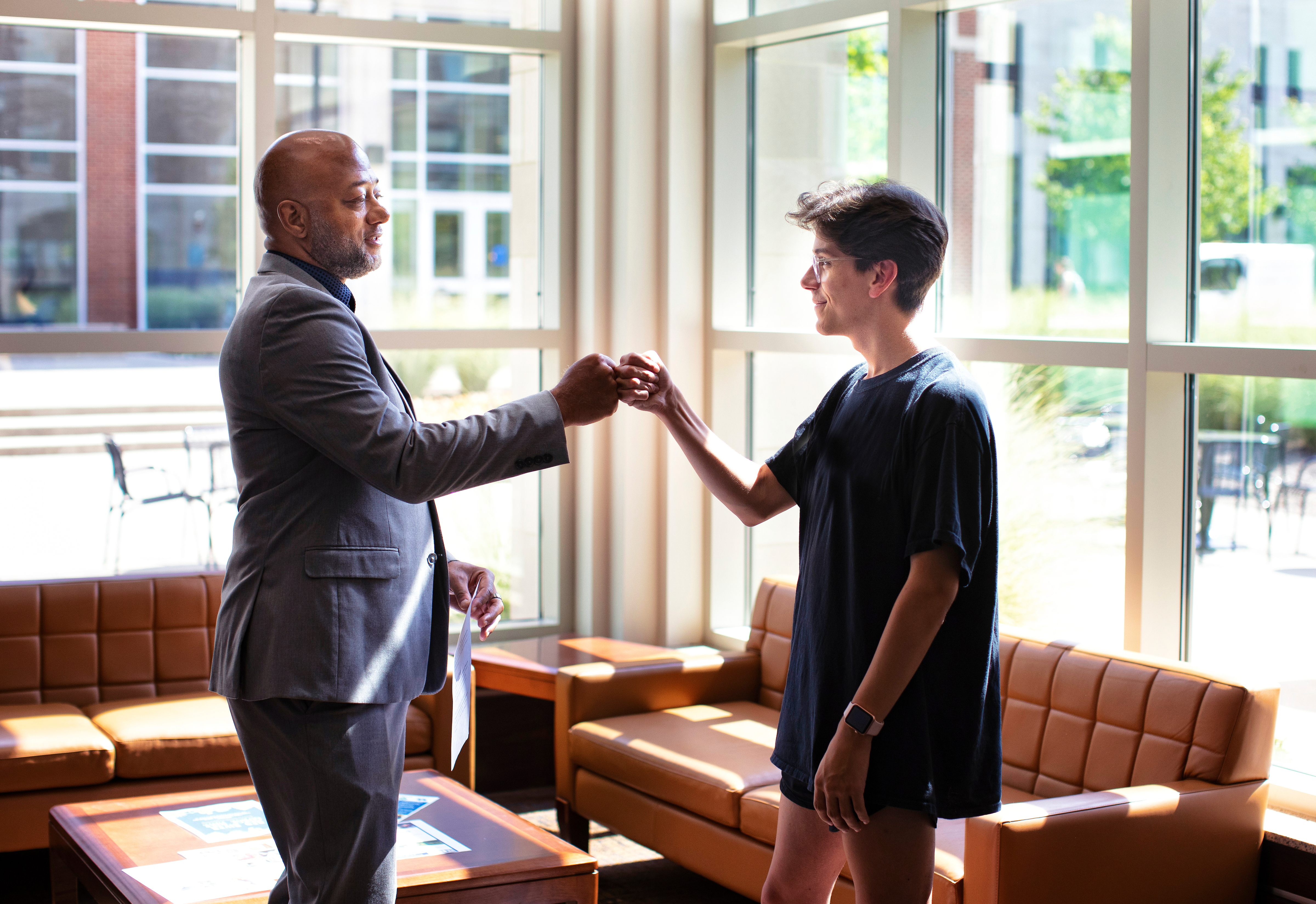 Student and professor fist bumping in lobby of Lewis Hall