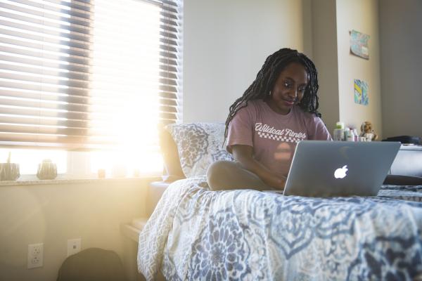 Photo of student sitting on residence hall bed with her laptop