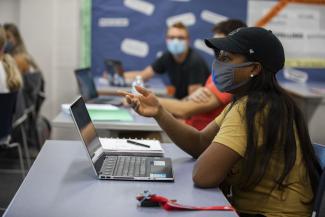 Students wear masks while sitting physically distanced in a classroom.