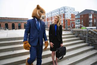 UK mascot in a business suit walking down the stairs speaking with a woman also in a business suit.