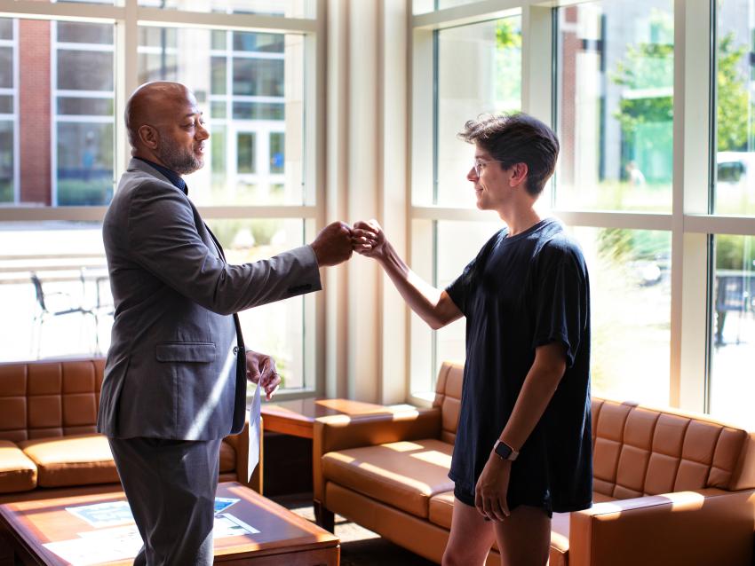 Student and professor fist bumping in lobby of Lewis Hall