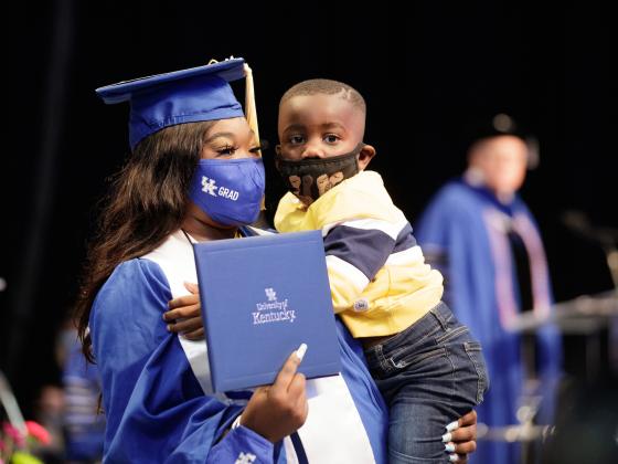 Woman at Commencement holding a degree and child.